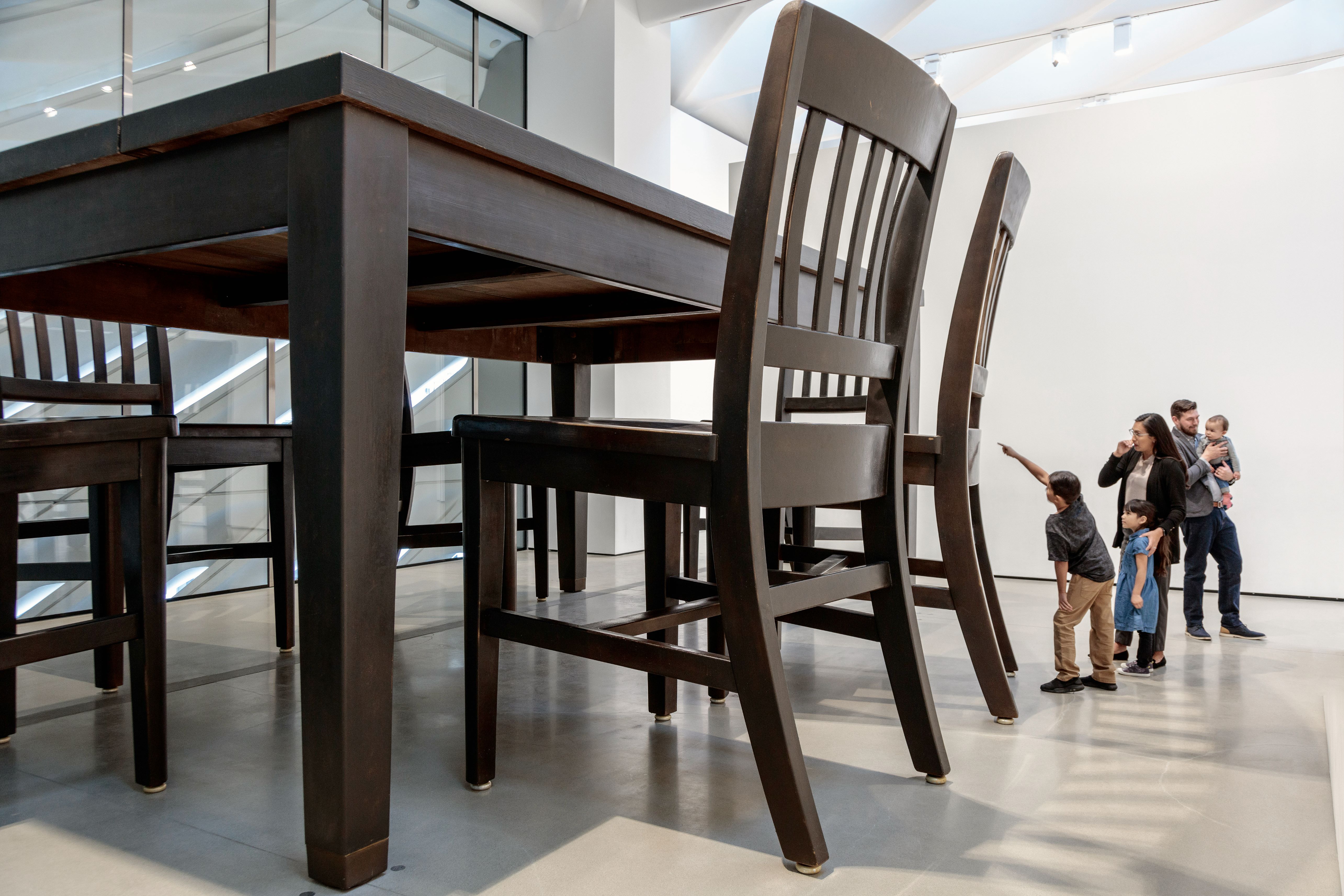 Photo of Robert Therrien's Under The Table sculpture, which is an oversized brown wooden table, with a family of five next to it for scale.