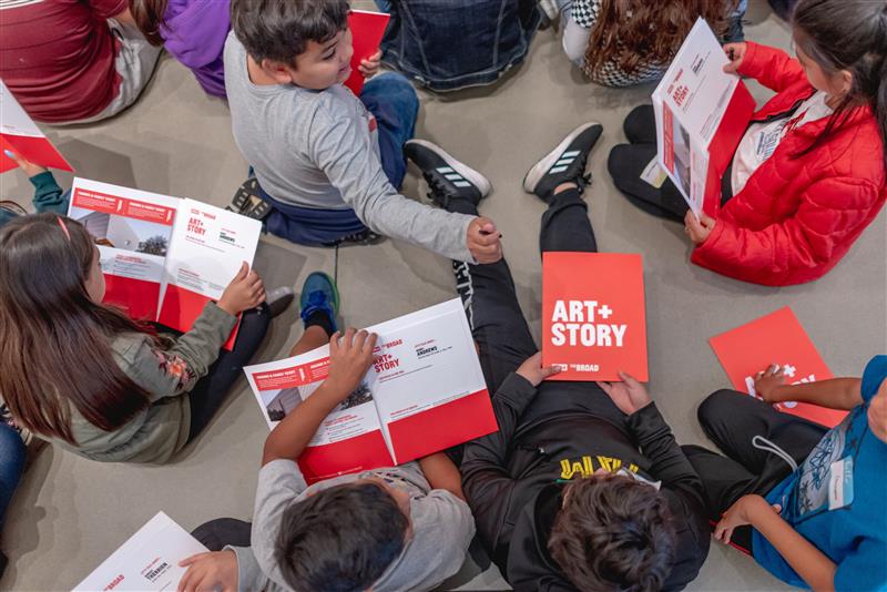 Children sitting on the floor at The Broad holding red folders that say ART + STORY