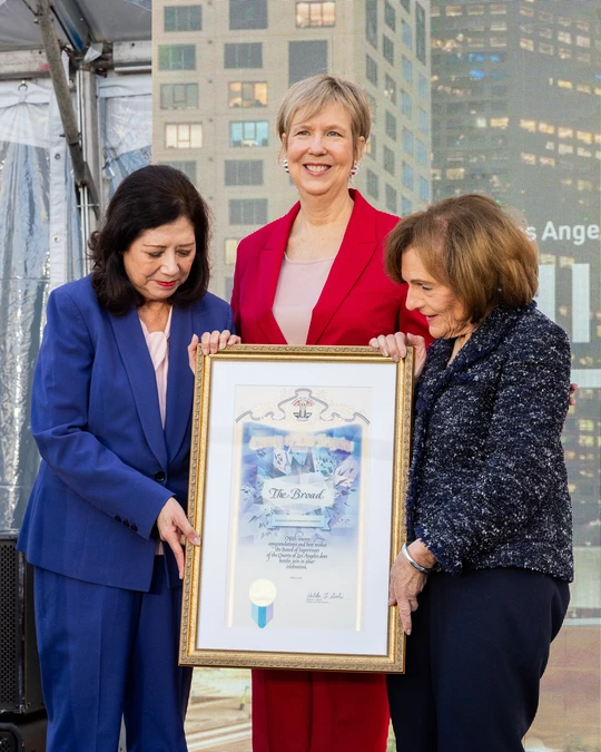 Three women standing in suits, holding a framed image