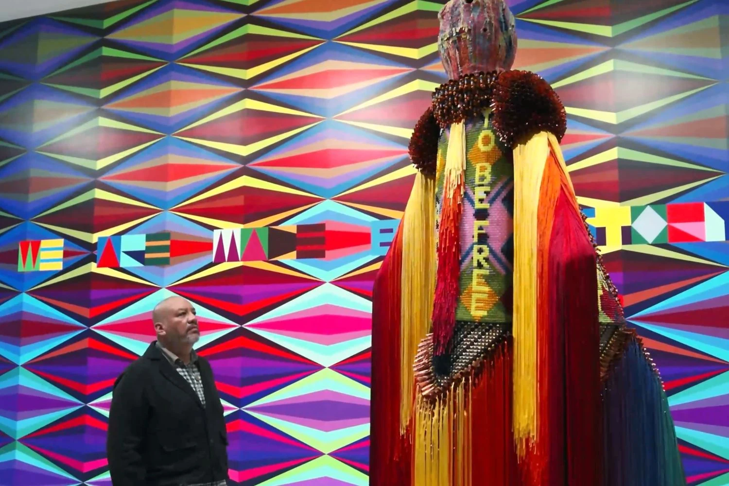 Jeffrey Gibson inside his exhibition at The Broad looking at a tall sculpture