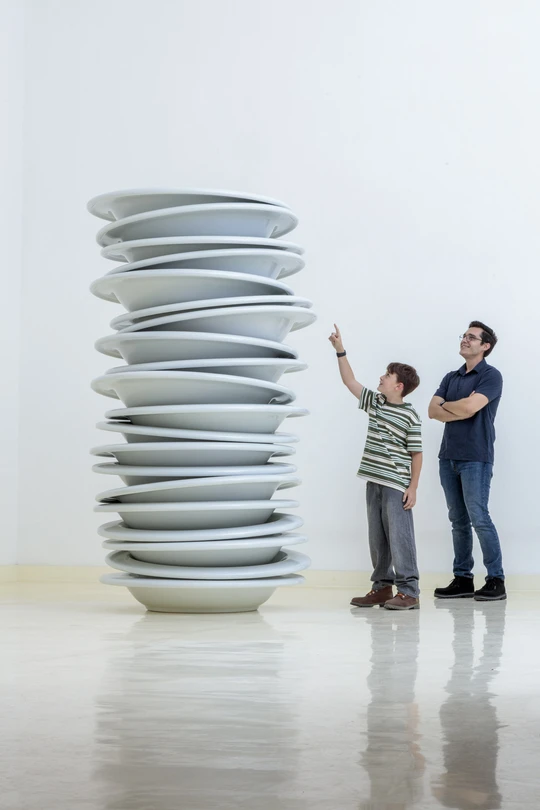 Man with a young boy standing next to Robert Therrien's sculpture of an oversized stack of white plates